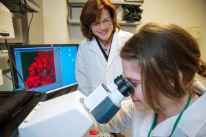 Dr. Lisa Cunningham in her lab smiling at a lab member who is using a microscope.